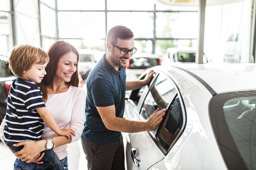 happy family looking at white car at dealership