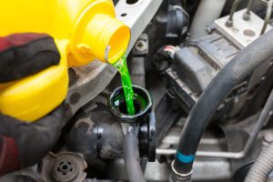 yellow bottle pouring green coolant into car radiator