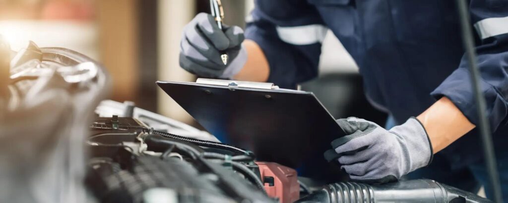 Mechanic writing on a clipboard during a car engine inspection