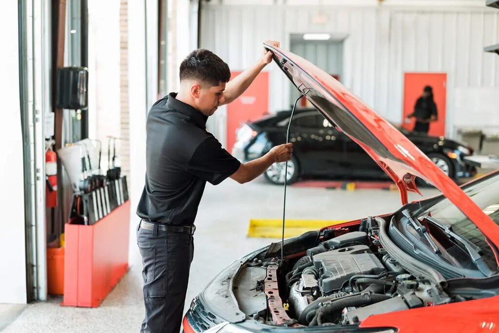 Mechanic checking the oil level of a red car inside an auto service shop.