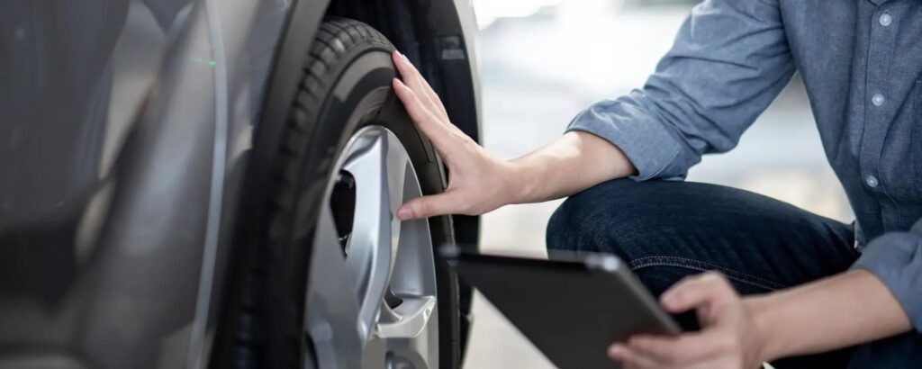 Person inspecting a car tire with a tablet.